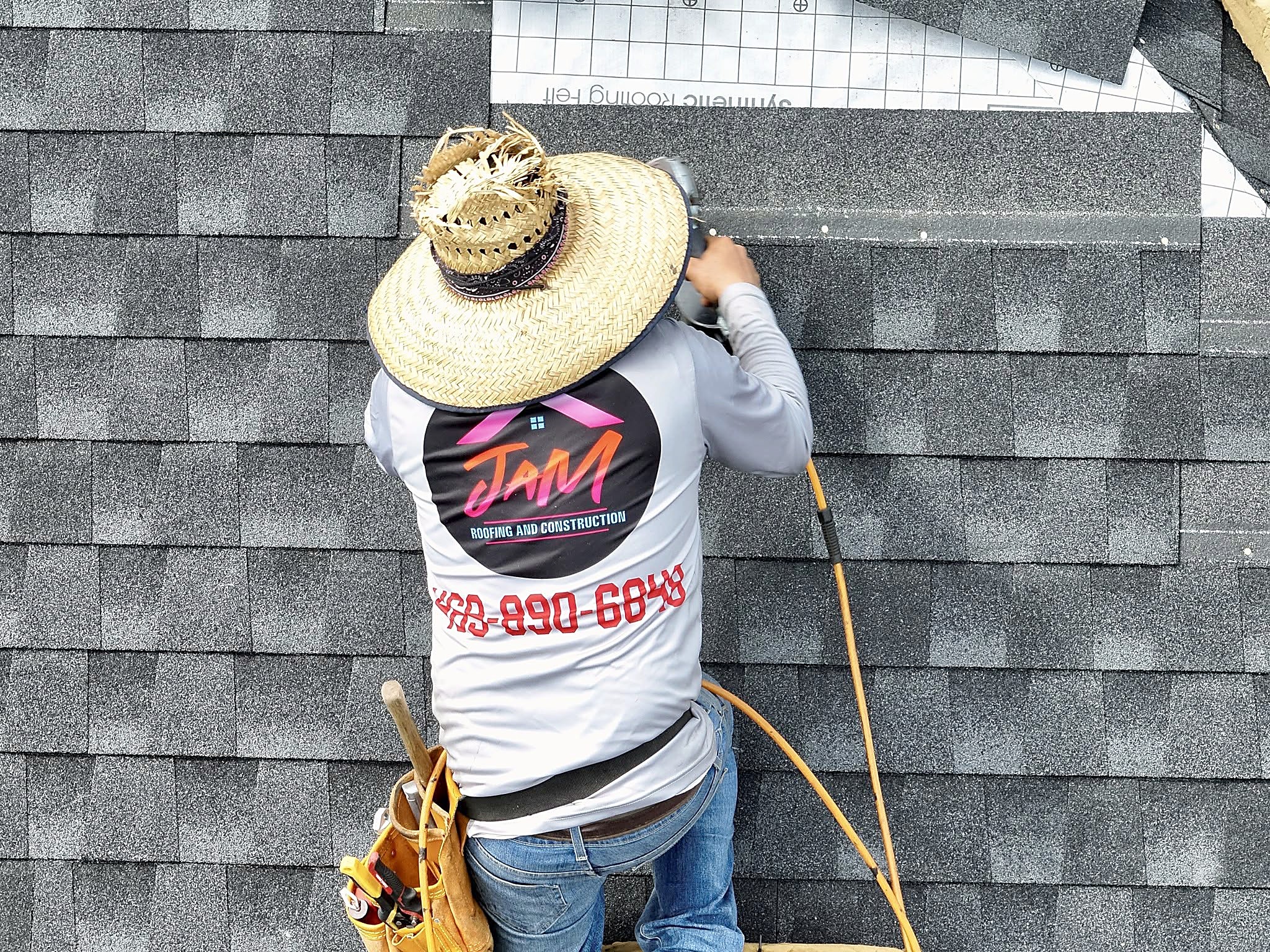 A roofer in a JaM Roofing shirt setting shingles with a nail gun