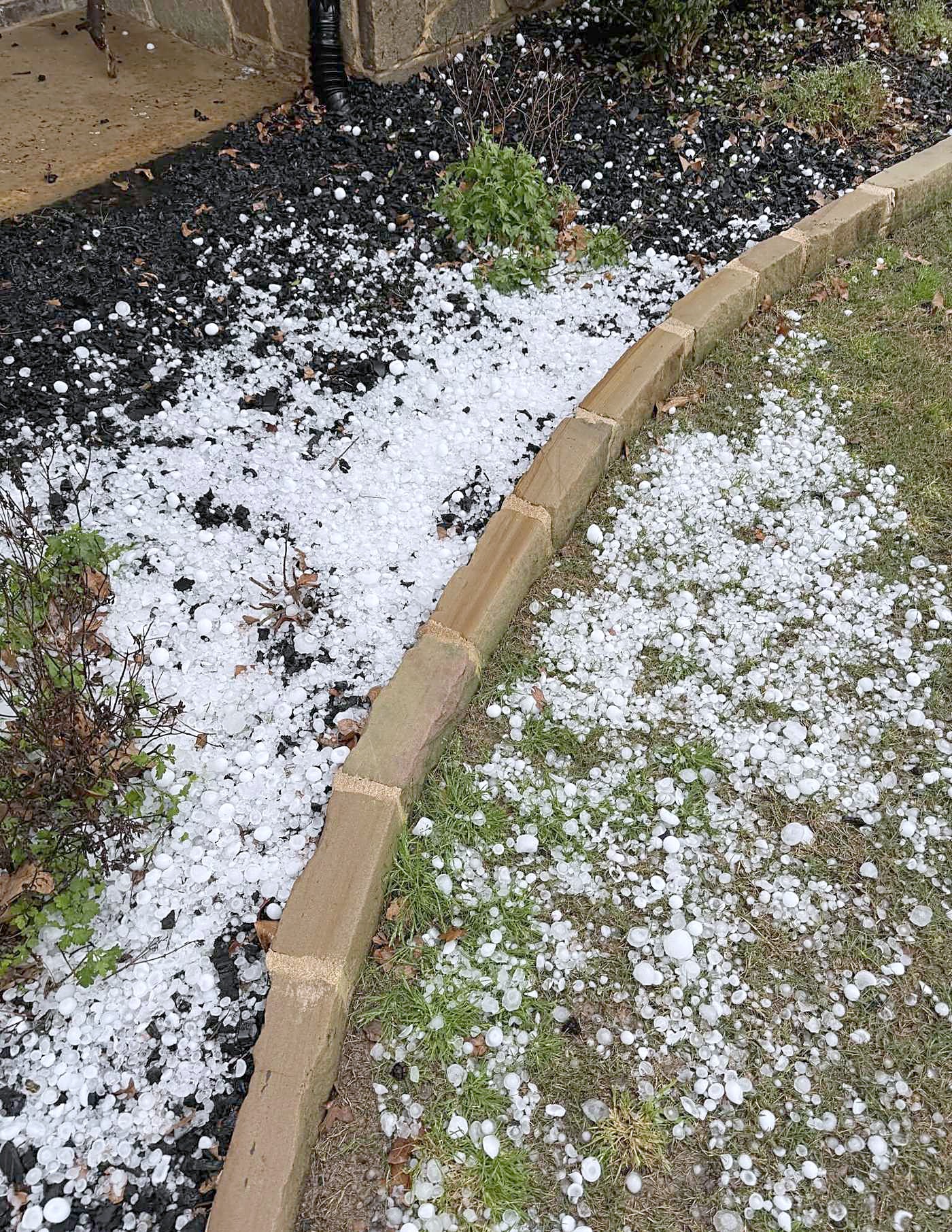 Hailstones piled along a stone garden border after a storm