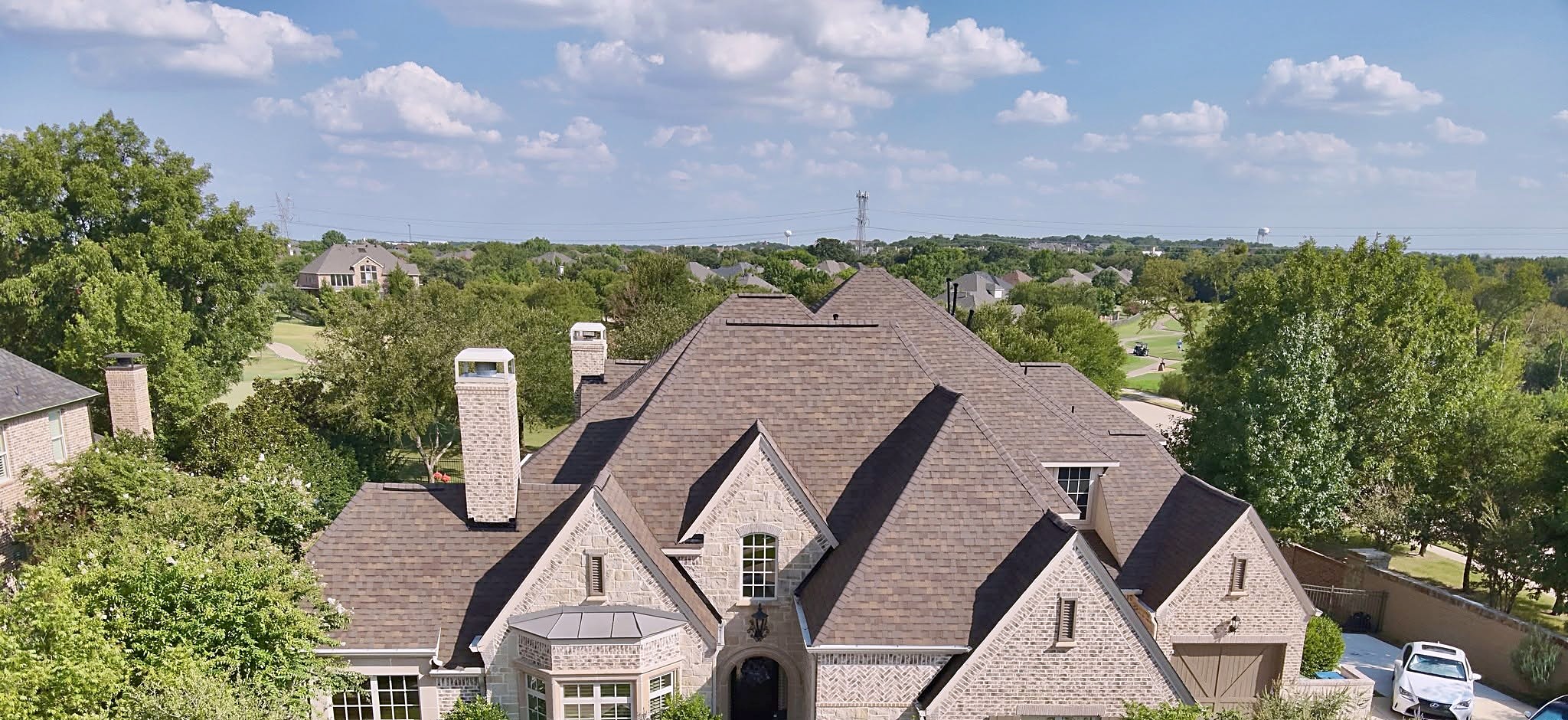 An aerial view of a two-story brick home with a new shingle roof and a pool in the back yard