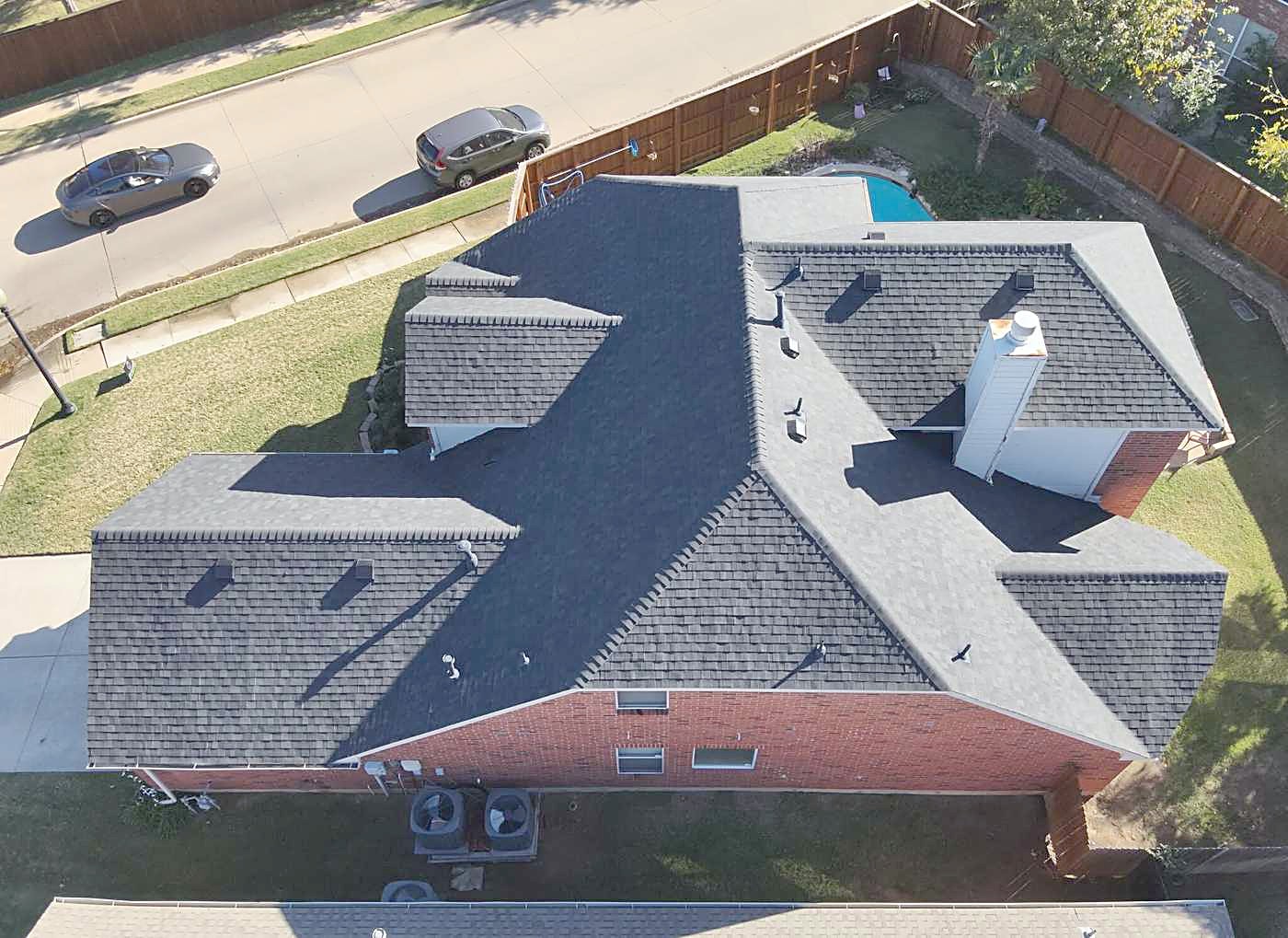 An aerial view of a finished shingle roof on a single-story brick home