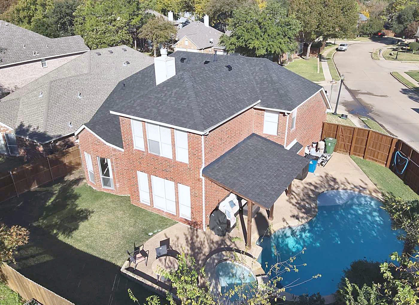 An aerial view of a two-story brick home with a finished shingle roof and a pool in the back yard