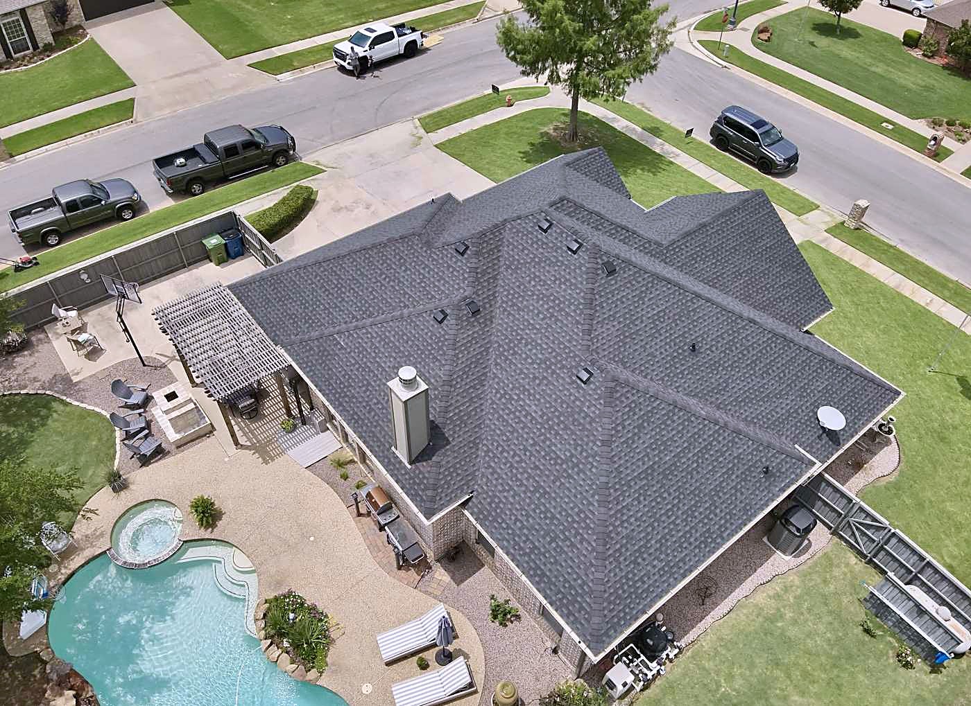 An aerial view of a finished roof on a home with a pool and covered patio