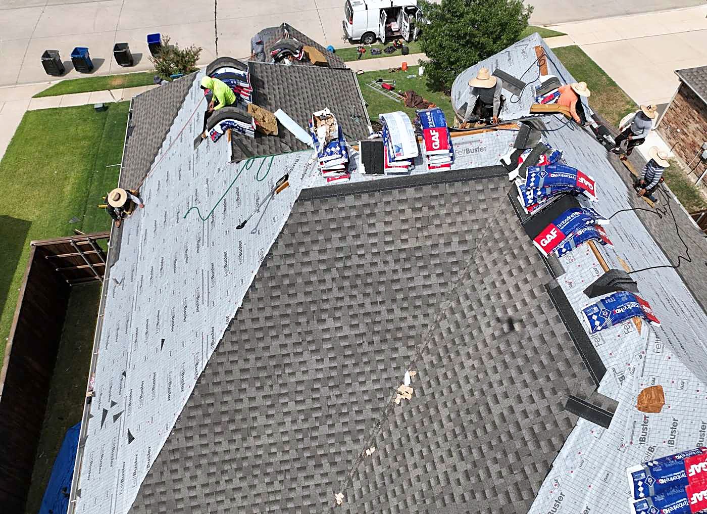An aerial view of a roof half stripped to the underlayment with shingle bundles stacked on it